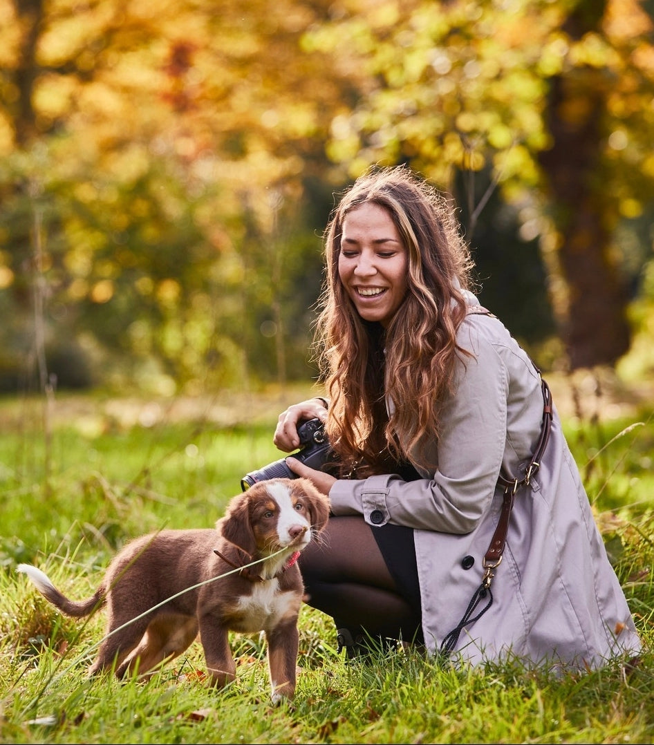 Fotografin mit Hund beim Outdoor-Shooting – stilvoller Leder-Kameragurt für aktive Frauen.
